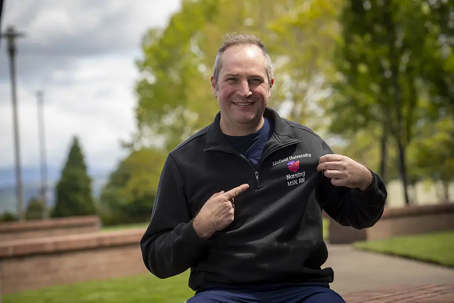 Photo of Ryan on the Linfield Portland campus pointing to the Linfield logo on his sweater.