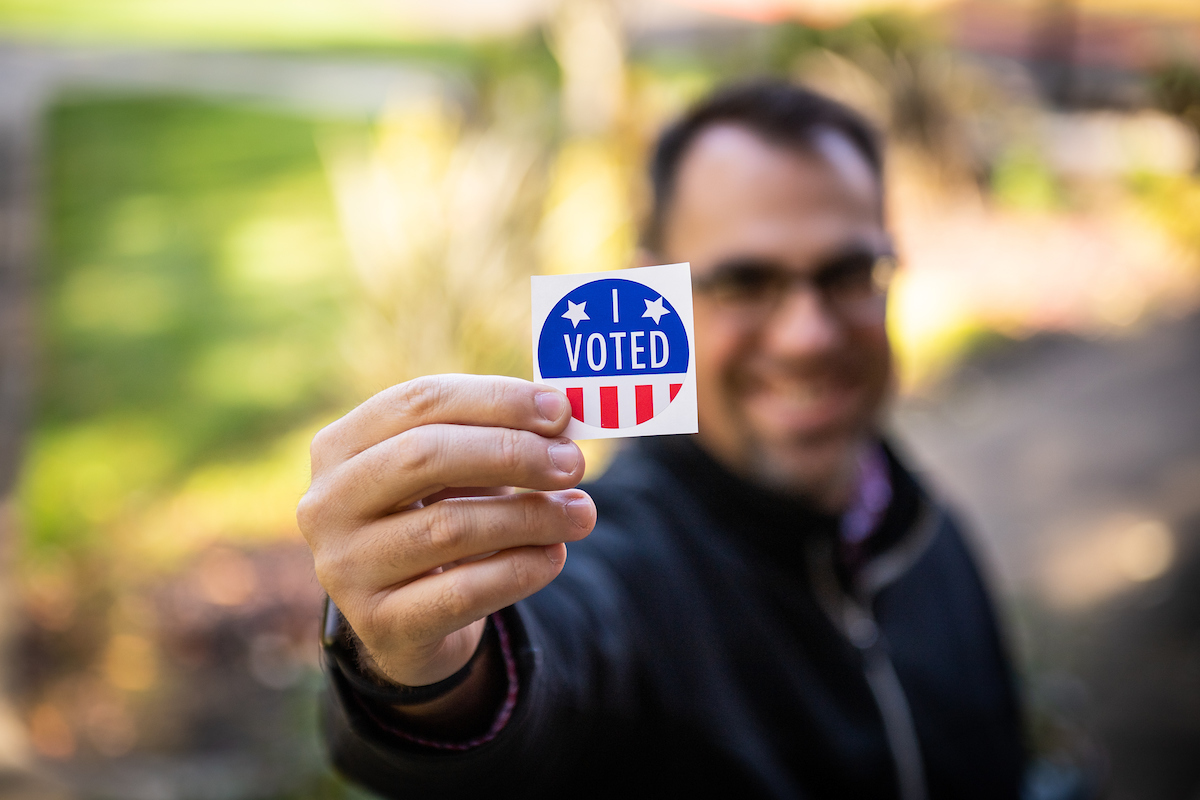 Linfield community member holding up a "Vote!" sticker.