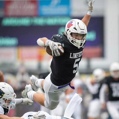 Linfield football player catching a pass and jumping over the defensive line..