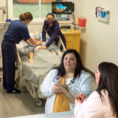 Nurse leader in white lab coat holding clipboard while observing students in a simulation.