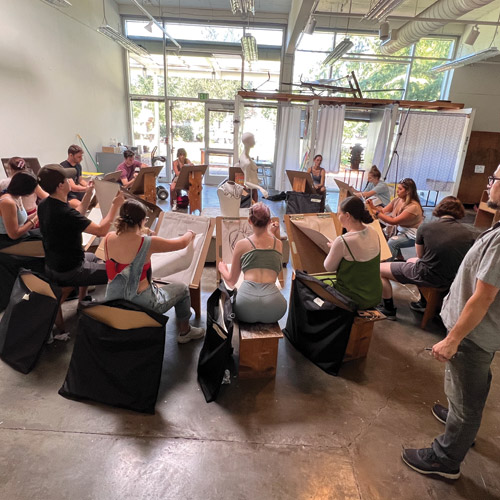 students drawing on easels sitting in a circle with Professor Serhat Tanyolacar