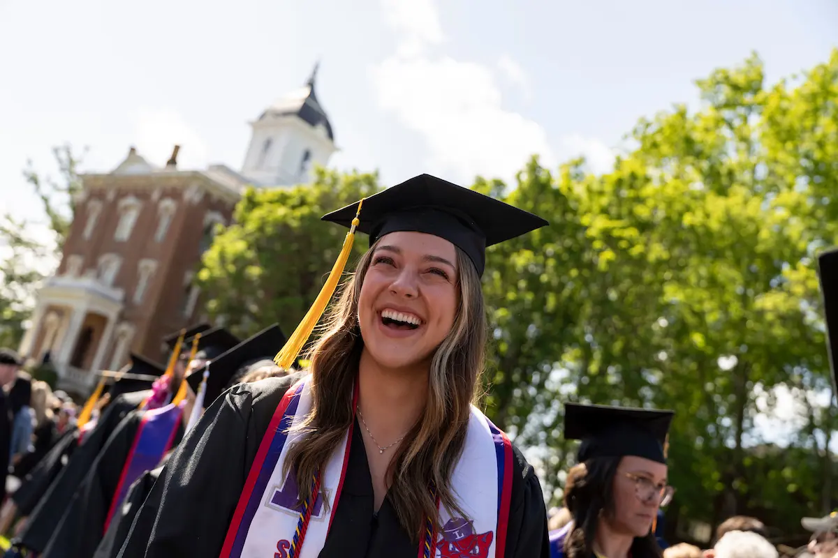 Female graduate smiles in regalia at 2024 Commencement