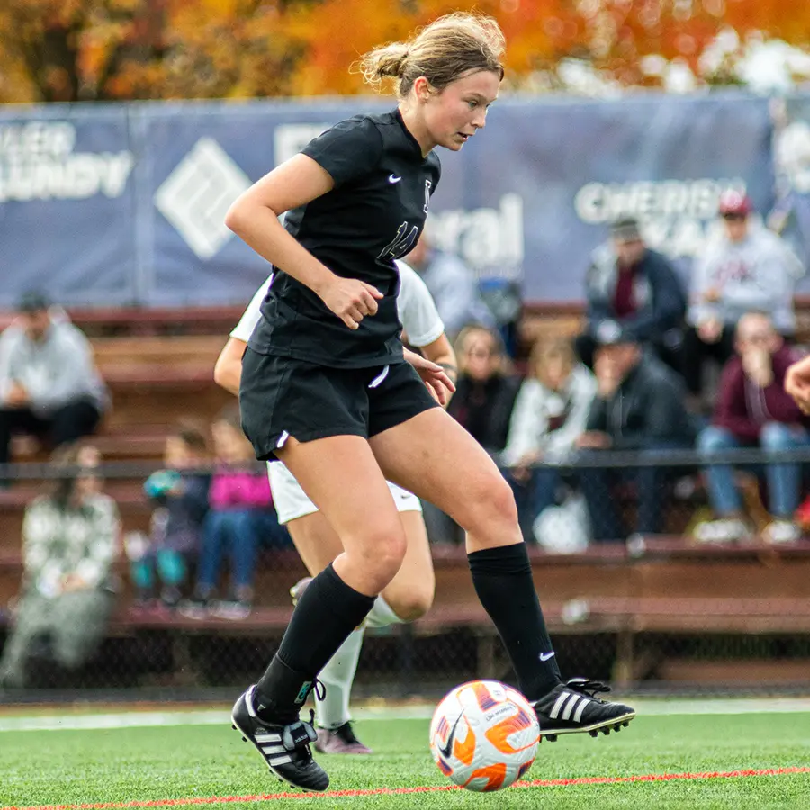 Linfield women's soccer player dribbling between defenders.